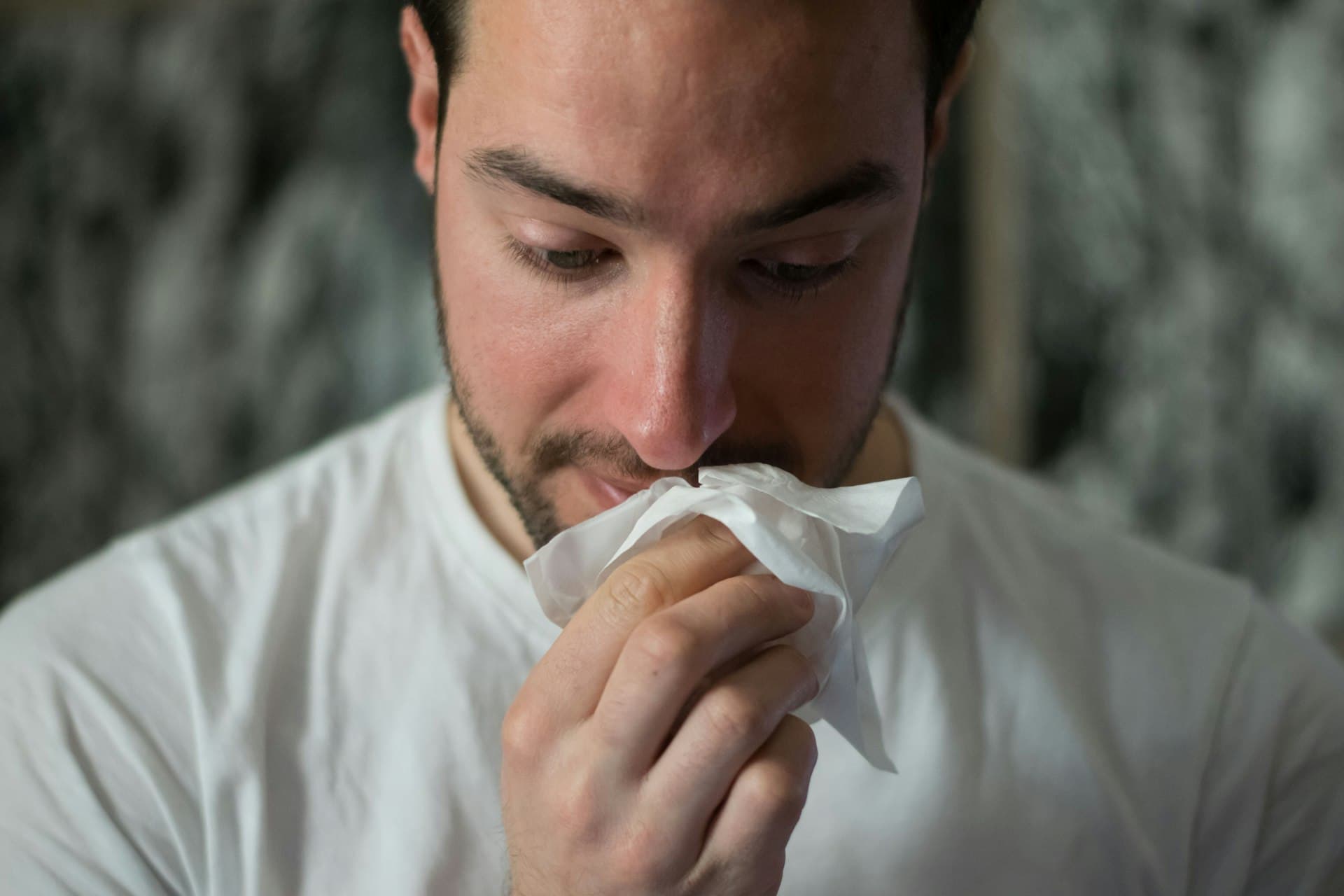Person with allergy symptoms blowing their nose at home